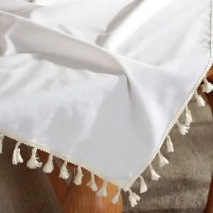 Detailed close-up of white cotton tablecloth fabric with decorative tassel edge