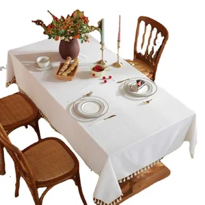 Thick rectangular off-white tablecloth with elegant tassel edges on a wooden table