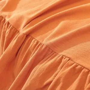 Macro detail of orange linen sofa cover with elegant ruffle edge and breathable texture