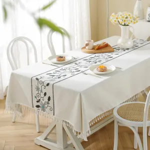 Detailed view of beige rectangular tablecloth with floral patterns and white tassels