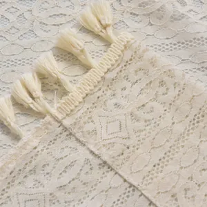 Macro detail of beige hollow lace fabric with intricate patterns and soft fringe trim