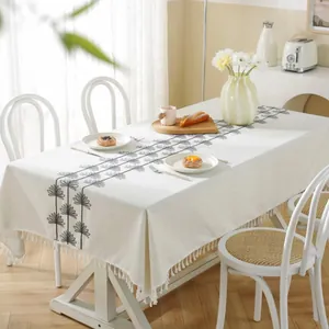 Detail of beige rectangular tablecloth with black leaf embroidery and fringe tassels