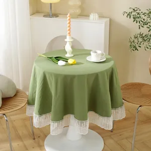 Olive green round cotton tablecloth with white lace border on a wooden dining table