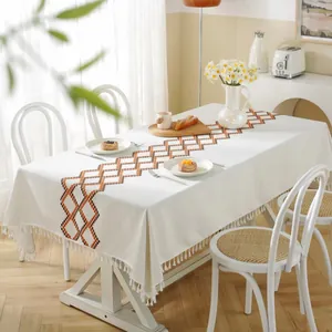 Close-up of geometric diamond weave pattern and white fringe tassels on linen tablecloth