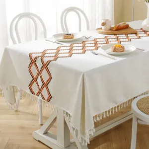 Detail of beige Christmas tablecloth featuring orange geometric pattern and white tassels