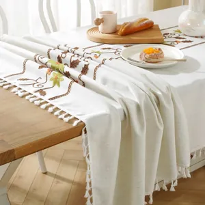 Close-up of beige table runner featuring floral embroidery and delicate tassel edges