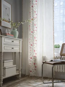 Detail of floral embroidery and pompom tassel trim on semi-sheer linen curtain
