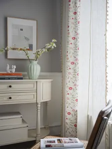 Detail of floral embroidery and beige tassel trim on elegant semi-sheer linen curtains