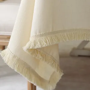 Close-up of cream linen tablecloth featuring intricate fringe tassels and textured fabric