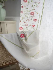 Detail of floral embroidery on cream linen curtains with elegant beige tassel edge