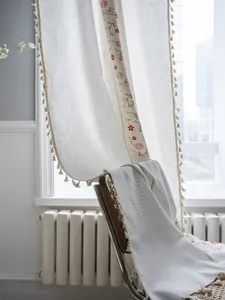 Detail showing colorful floral embroidery and pom-pom tassel fringe on linen curtain