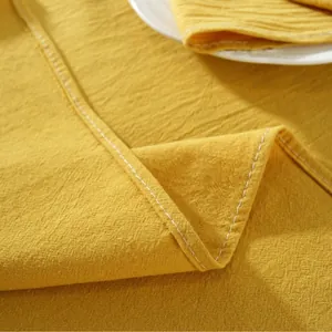 Close-up of ginger yellow cotton tablecloth with white decorative stitching and linen texture
