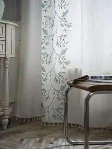 Detailed texture of green floral embroidery and beige tassel fringe on semi-sheer curtain