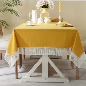 Detail van mosterdgeel tafelkleed met witte kanten randen op een houten eettafel