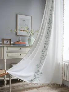 Close-up of white cotton linen curtain with green floral embroidery and tassel trim