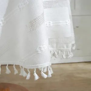 Close-up of white woven tablecloth with textured jacquard patterns and elegant fringe trim