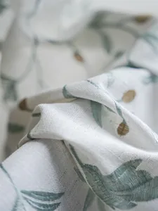 Close-up of green floral leaf embroidery on beige linen curtain fabric with detailed texture
