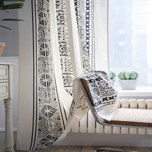 Bohemian black and white geometric linen curtain draped over a rattan chair in a sunlit room