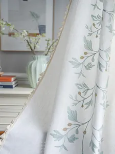 Detailed close-up of green botanical floral embroidery and beige tassels on cotton linen curtains