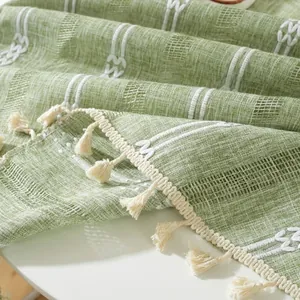 Close-up of sage green woven tablecloth with white geometric embroidery and fringe tassels
