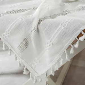 Detail of white hollowed jacquard tablecloth with elegant tassels on a wooden surface