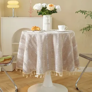 Detail of round beige tablecloth with white stripes, rhombic patterns and tassel fringe