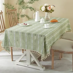 Green striped jacquard tablecloth with elegant white fringe tassels in a cozy dining setting