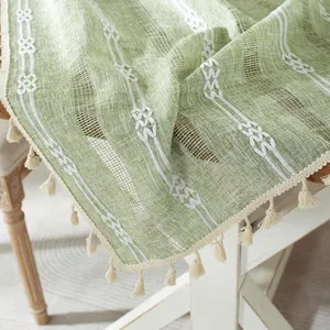 Macro detail of green jacquard table runner with white flower embroidery and cotton tassels