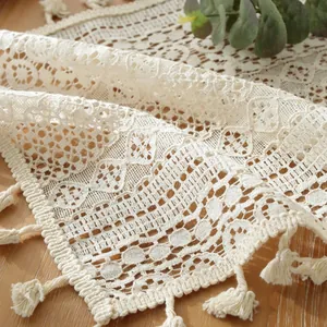 Gros plan d'un chemin de table en dentelle ivoire avec motifs floraux et franges