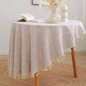 Close-up of beige plaid round tablecloth with tassel edge and textured faux linen fabric
