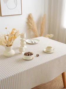 Detail van gestreept crème katoen-linnen tafelkleed met elegant keramisch servies en decor