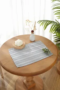 Close-up of light gray striped placemat with fringe details on a wooden dining table