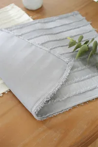 Close-up of grey textured fabric placemat with decorative fringe and stripe details