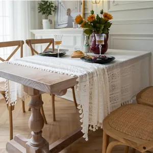 Detail showing beige lace tablecloth with hollow weave and pom-pom fringe on wooden table