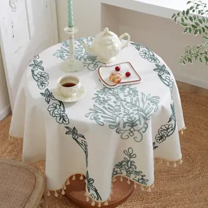 Detalle de mantel de jacquard beige con bordado floral verde y borde de borlas