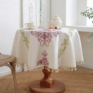 Detalle de mantel redondo de lino beige con bordado floral y bordes decorados con borlas
