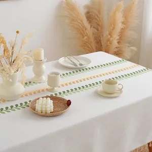Rectangular white linen tablecloth with green leaf embroidery and fringed edges