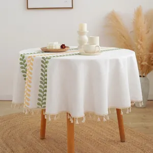 Mantel redondo blanco con patrones de hojas amarillas y verdes y elegantes borlas