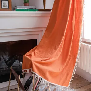 Dettaglio della tenda in cotone arancione con nappe decorative accanto al camino bianco