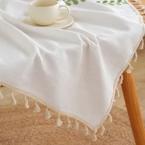 Detailed close-up of beige linen tablecloth with green leaf embroidery and fringe edges