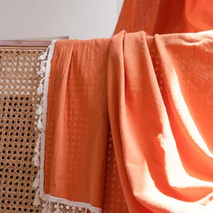 Coperta in cotone arancione con nappe bianche adagiata su sedia in rattan