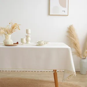 Detailed close-up of cream cotton linen tablecloth with fringe tassels on wood table