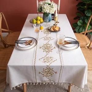 Detailed close-up of beige linen tablecloth featuring gold embroidery and tassel trim