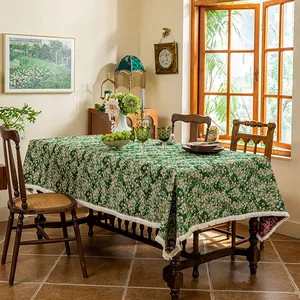 Detailed close-up of dark green floral tablecloth with decorative white tassel edges