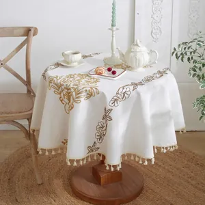 Detalle de bordado floral marrón y flecos de borlas beige en el mantel redondo de lino