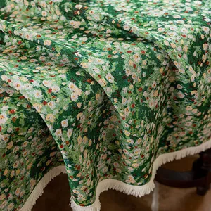 Detail of green floral jacquard tablecloth featuring white daisies and white fringe edges