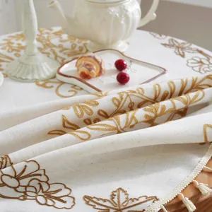 Detalle del bordado floral barroco nórdico en mantel de lino con flecos dorados