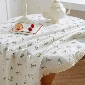 Detailed embroidery of daisies on a beige linen tablecloth featuring fringed edges