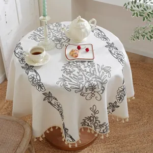 Primer plano de mantel redondo beige con bordado floral gris y elegantes bordes de flecos