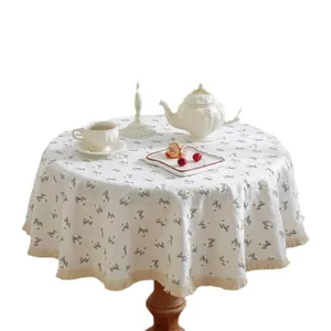 Round cream linen tablecloth with daisy embroidery and elegant fringe tassels on wooden table